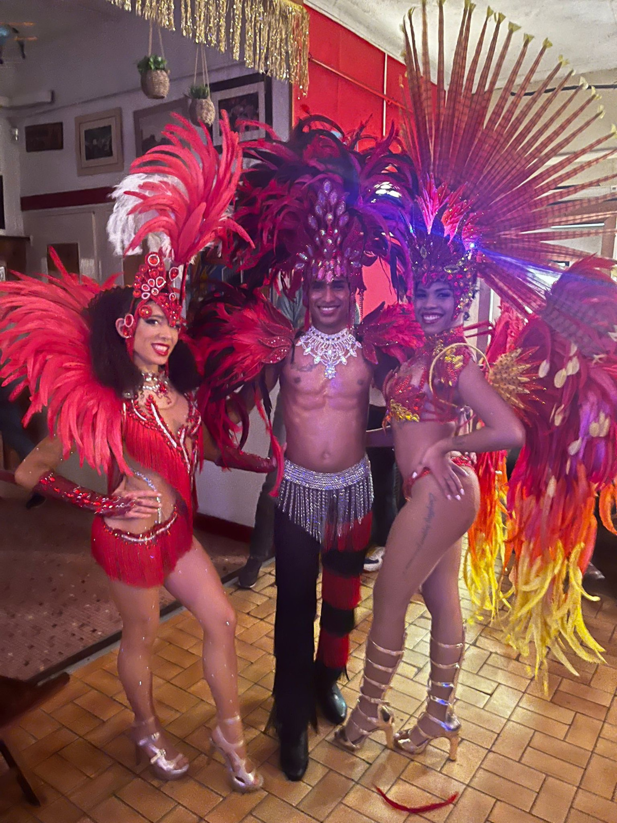 Danseuses en costumes samba à grandes plumes rouges et jaune avec un danseur torse nu et avec des plumes